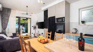 A modern kitchen with a dining area, a sofa, and a bottle of wine. - Apartments Tomas (Omis)
