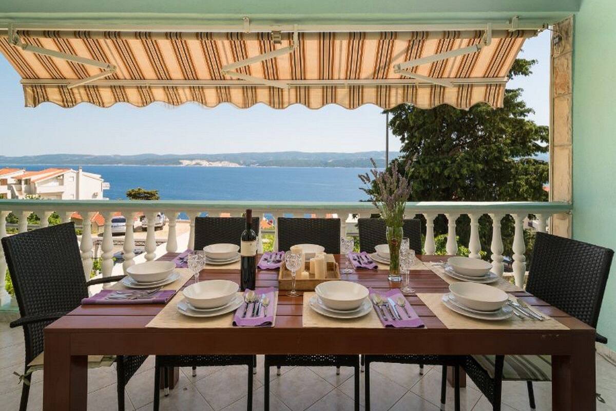 A dining table set for four with a view of the sea and hills in the background.