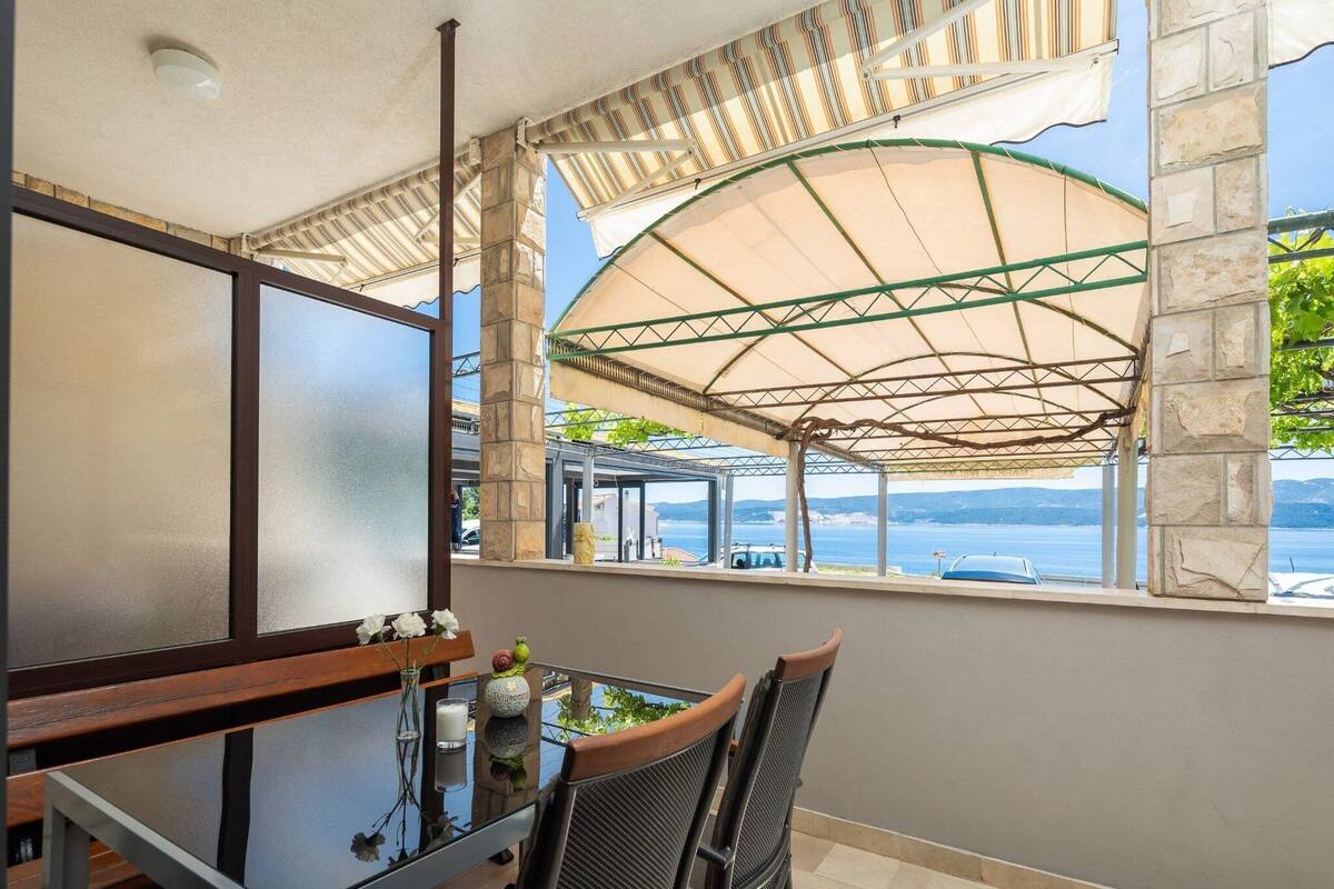 A balcony with a glass table, two chairs, and a view of the sea.