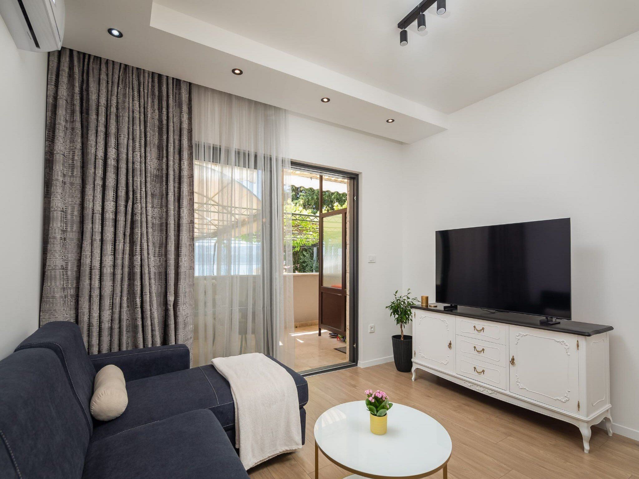 A modern living room with a dark sofa, a white coffee table, a TV, and a white cabinet.