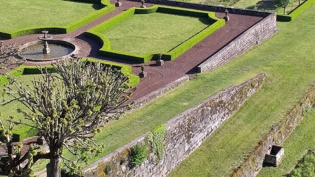 Un jardin à la française, avec des haies aux formes géométriques, une fontaine centrale et des murs en pierre.