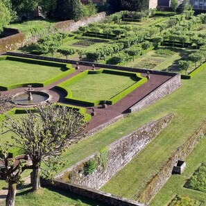A formal garden with geometric hedges, a central fountain, and stone walls.