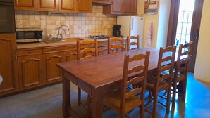 Une cuisine avec des meubles de rangement en bois, un four à micro-ondes, une cuisinière à gaz et une table à manger avec des chaises.