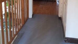 Un couloir étroit avec des rampes en bois, un luminaire au plafond et une porte donnant sur une pièce où se trouvent une table et des chaises.