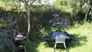 Un espace extérieur aménagé pour les repas, avec un mur en pierre et un barbecue.