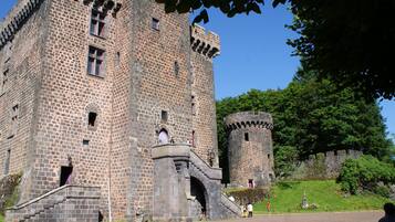 Un château historique en pierre, doté d’une tour imposante, d’une grande entrée en arc de cercle et entouré d’un paysage verdoyant.