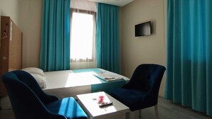 Habitación de hotel con cama, dos sillas, una mesita, televisión y ventana con cortinas.