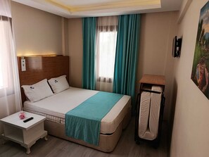 Quarto de hotel com cama, mesa de cabeceira, cortinas na janela e um quadro na parede.