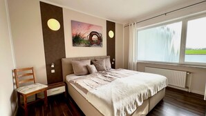 Ein Schlafzimmer mit Bett, Stuhl, einem Bild und einem Fenster mit Blick.