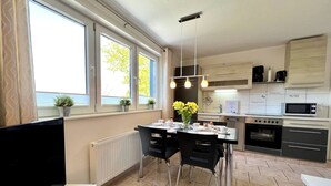 A modern kitchen with a dining area, large windows, and a view of the sea.