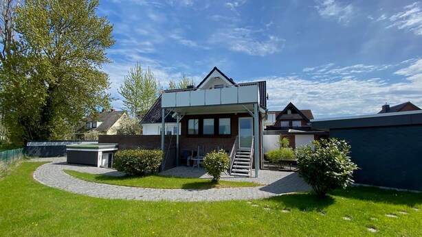 A modern house with a covered patio, a small outdoor seating area, and a well-maintained lawn.