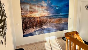 A room with a large wall mural of a beach scene, a wooden staircase, and a modern light fixture.