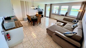 A modern living room with a sofa, a dining table with chairs, a TV, and a view of the outdoors. - Well-kept vacation complex with 5 residential units in a quiet cul-de-sac location (Dahme)