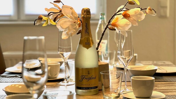 Et bord dækket med en flaske Freixenet champagne, to vaser med blomster og flere vinglas.