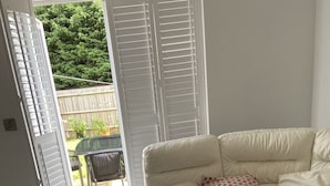 A living room with a beige sofa, a glass coffee table, and a sliding glass door leading to a patio with a table and chairs. - Captivating 2-bed House in Wolverhampton (Wolverhampton)