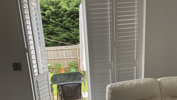 A room with a white leather sofa, a black throw pillow, and a patterned pillow. There is a small table with chairs outside the door. - Captivating 2-bed House in Wolverhampton (Wolverhampton)