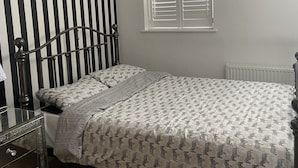 A bedroom with a bed, a dresser, a radiator, a window with blinds, and a striped wall. - Captivating 2-bed House in Wolverhampton (Wolverhampton)