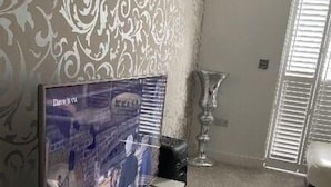 A living room with a flat-screen TV on a stand, a decorative wall, a large vase, and a door with blinds. - Captivating 2-bed House in Wolverhampton (Wolverhampton)