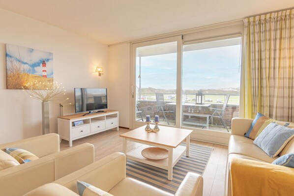 A modern living room with a flat-screen TV, a sofa, a coffee table, and a view of a golf course through large sliding glass doors.