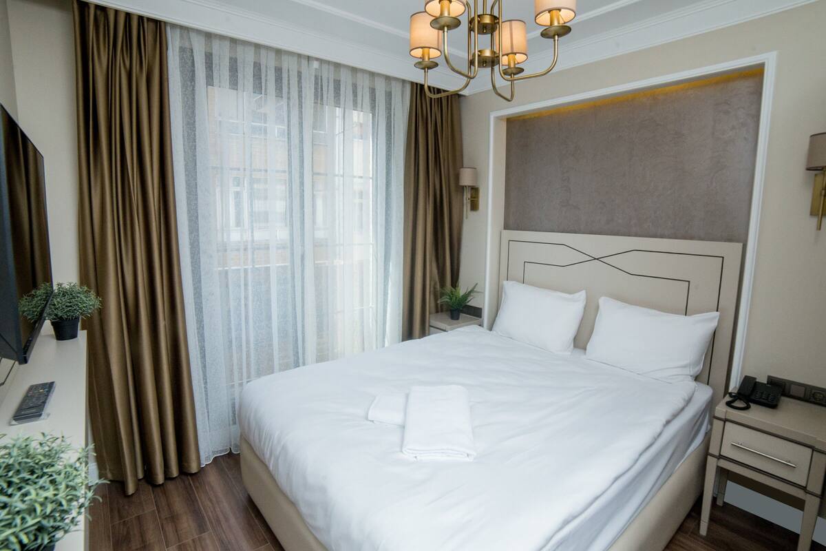Une chambre d’hôtel avec un grand lit, une table de chevet, une lampe et une fenêtre avec des rideaux.
