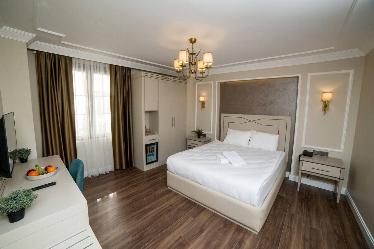 Une chambre d’hôtel comprenant un lit, des tables de chevet, un bureau avec une chaise, une télévision et une fenêtre avec des rideaux.
