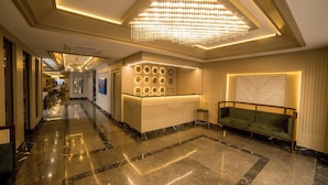 A hotel lobby with a marble floor, a reception desk, a green sofa, and a chandelier.