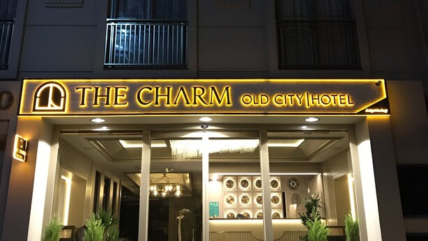 The exterior of The Charm Old City Hotel with illuminated signage, a grand entrance, and a modern facade.