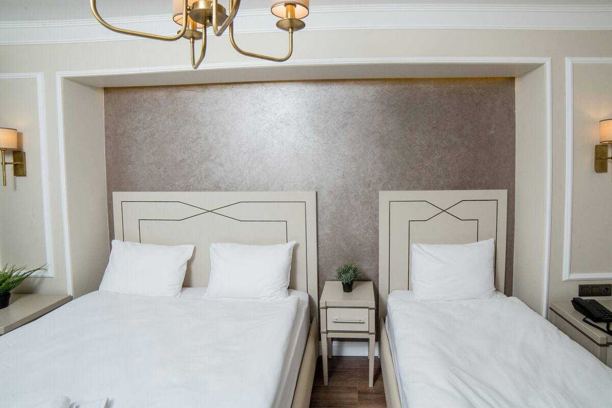 Une chambre d’hôtel avec deux lits, une petite table de chevet avec une lampe et un luminaire fixé au mur.