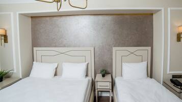 Een hotelkamer met twee bedden, een klein nachtkastje met een lamp en een wandlamp.