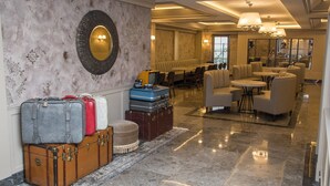 A lobby with a marble floor, a seating area with sofas and tables, and several suitcases stacked against the wall.