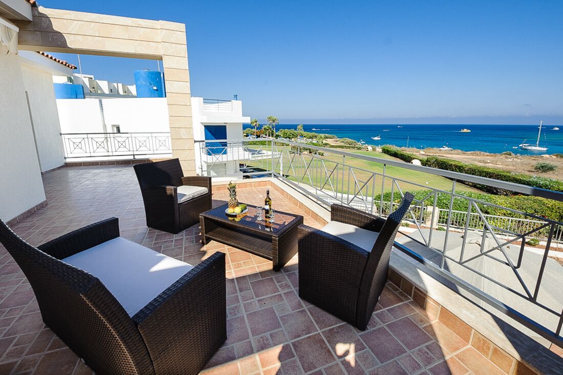 A balcony with wicker furniture, a small table, and a view of the ocean.