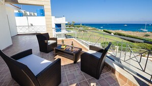 Ein Balkon mit Korbmöbeln, einem kleinen Tisch und Blick aufs Meer.