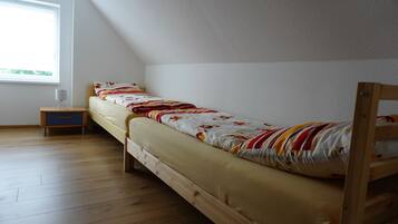 Ein Einzelbett mit Holzrahmen, ein kleiner Nachttisch und ein Fenster mit Tageslicht.