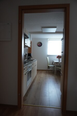 A narrow hallway leading to a kitchen with stainless steel appliances and a dining area with a table and chairs.