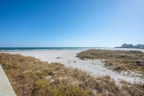 Uma praia com céu claro, areal arenoso e edifícios ao fundo.