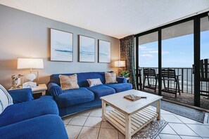 A living room with a blue sofa, a coffee table, and a view of the ocean through large windows.