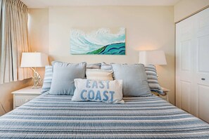 A bed with a striped blue and white bedspread, two pillows, a wall art piece, and a white door.