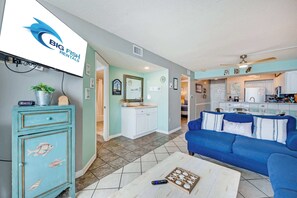 A living room with a blue sofa, a coffee table, and a TV displaying a logo.