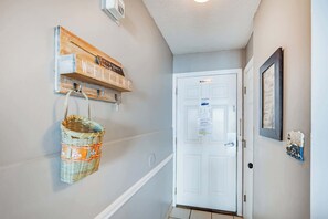 A hallway with a white door, a 'No Smoking' sign, a welcome sign, a wall-mounted basket, and a framed quote.