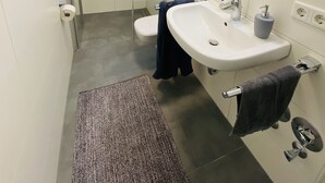 Un bany modern amb un espai de banyera de vidre, un lavabo blanc amb mirall i un suport per a tovalloles.