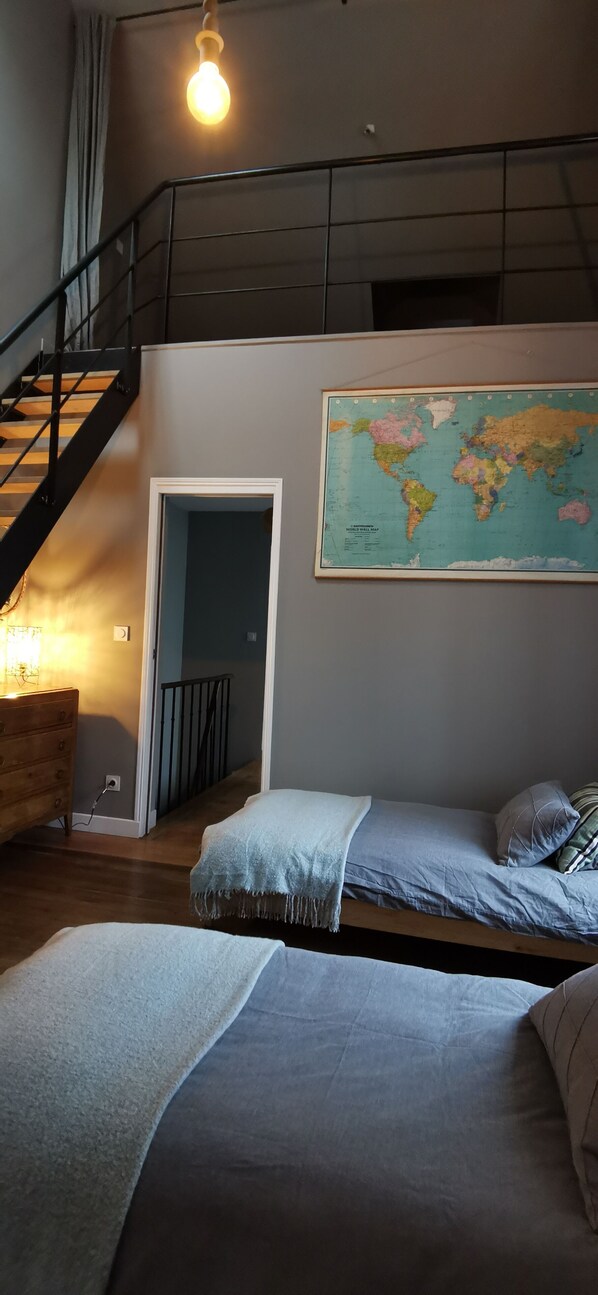 Un dormitorio con cama, cómoda, mapa en la pared y escalera.