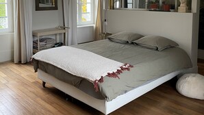 Une chambre à coucher comprenant un lit, une table de chevet, un miroir, une fenêtre avec des rideaux et un luminaire suspendu.
