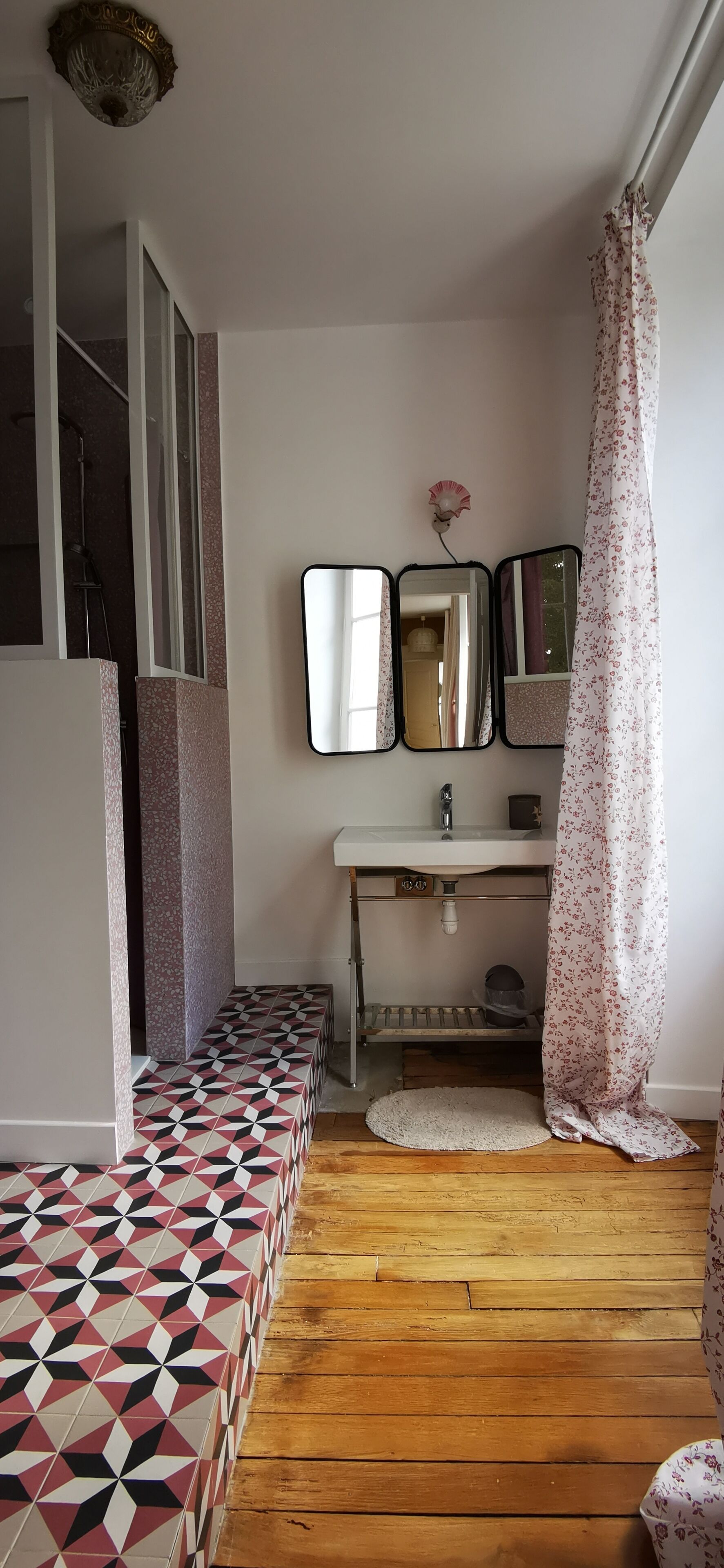 A bathroom with a geometric patterned floor, a white sink, and a mirror with a flower decoration.