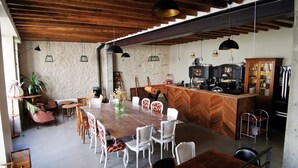 Un grand espace à manger avec une table en bois à motifs chevrons et des chaises blanches, un coin cuisine avec un dosseret à motifs chevrons et des luminaires suspendus.