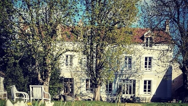 Un grand bâtiment historique doté de nombreuses fenêtres et d’un jardin bien entretenu, où l’on peut admirer des tulipes blanches au premier plan.