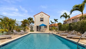 A swimming pool with lounge chairs and a building with a red roof in the background.