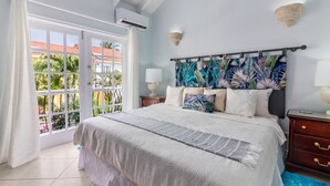 A bedroom with a large bed, a window with curtains, a nightstand, and a wall-mounted lamp.