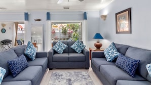 A living room with two grey sofas, patterned cushions, a ceiling fan, a lamp, and a framed picture on the wall.
