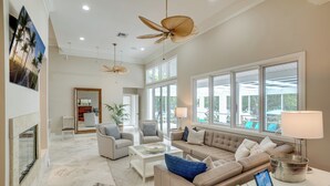 A spacious living room with a fireplace, large windows, and a ceiling fan. - Golf Cart, Bimini Cove by SeaBreeze Vacation (Anna Maria)