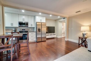 A modern kitchen with stainless steel appliances, wooden dining table, and white cabinetry.